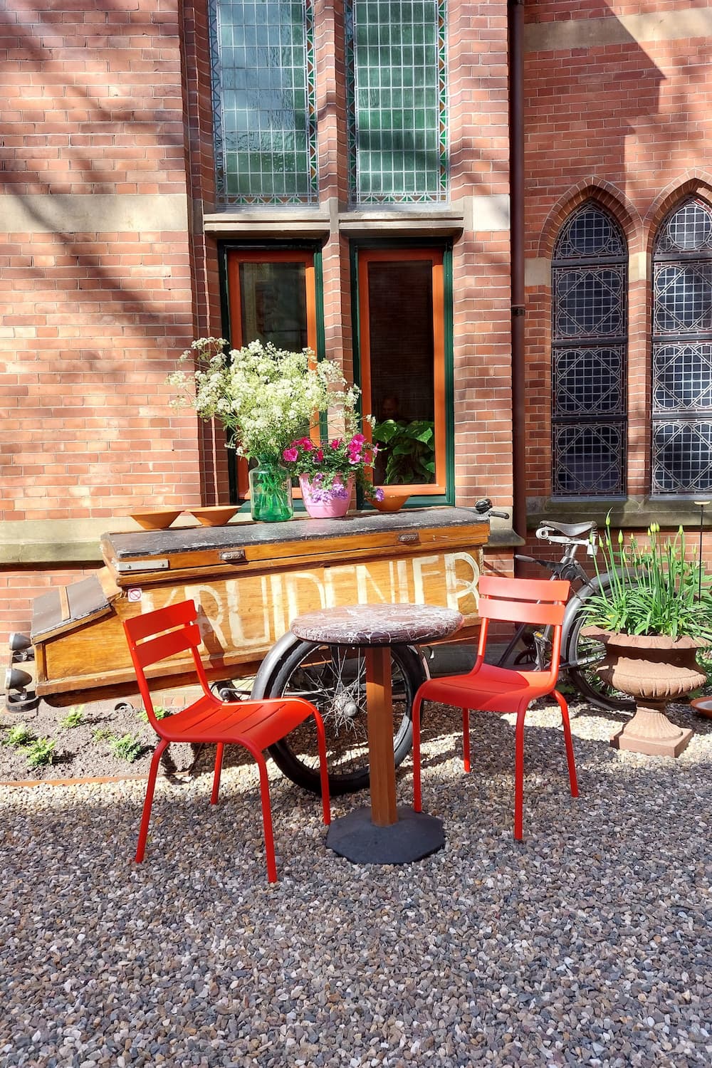 Binnentuin van Grand Café Staatsman, oude bakfiets op de achtergrond, tafeltje met twee rode stoelen