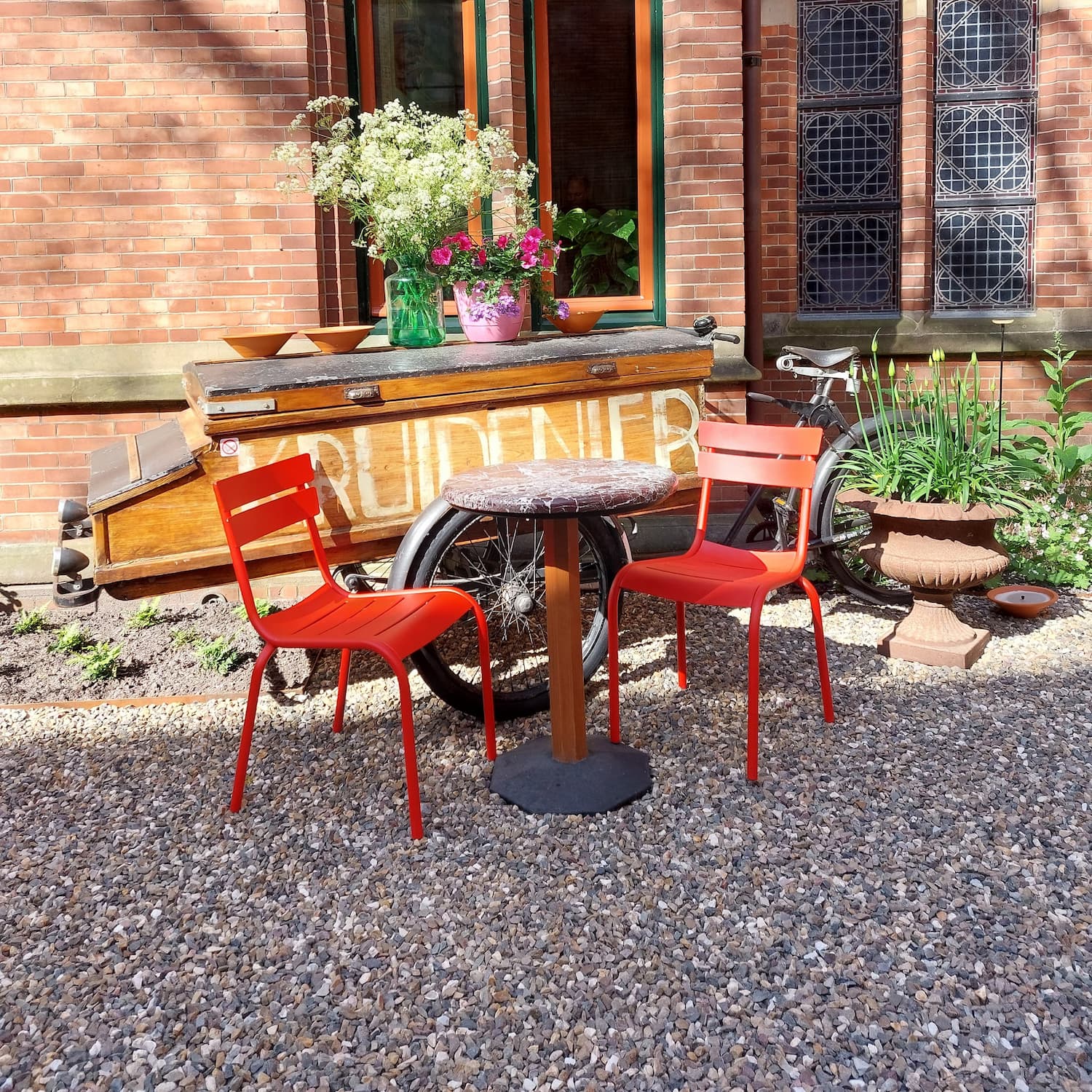 Binnentuin van Grand Café Staatsman, oude bakfiets op de achtergrond, tafeltje met twee rode stoelen